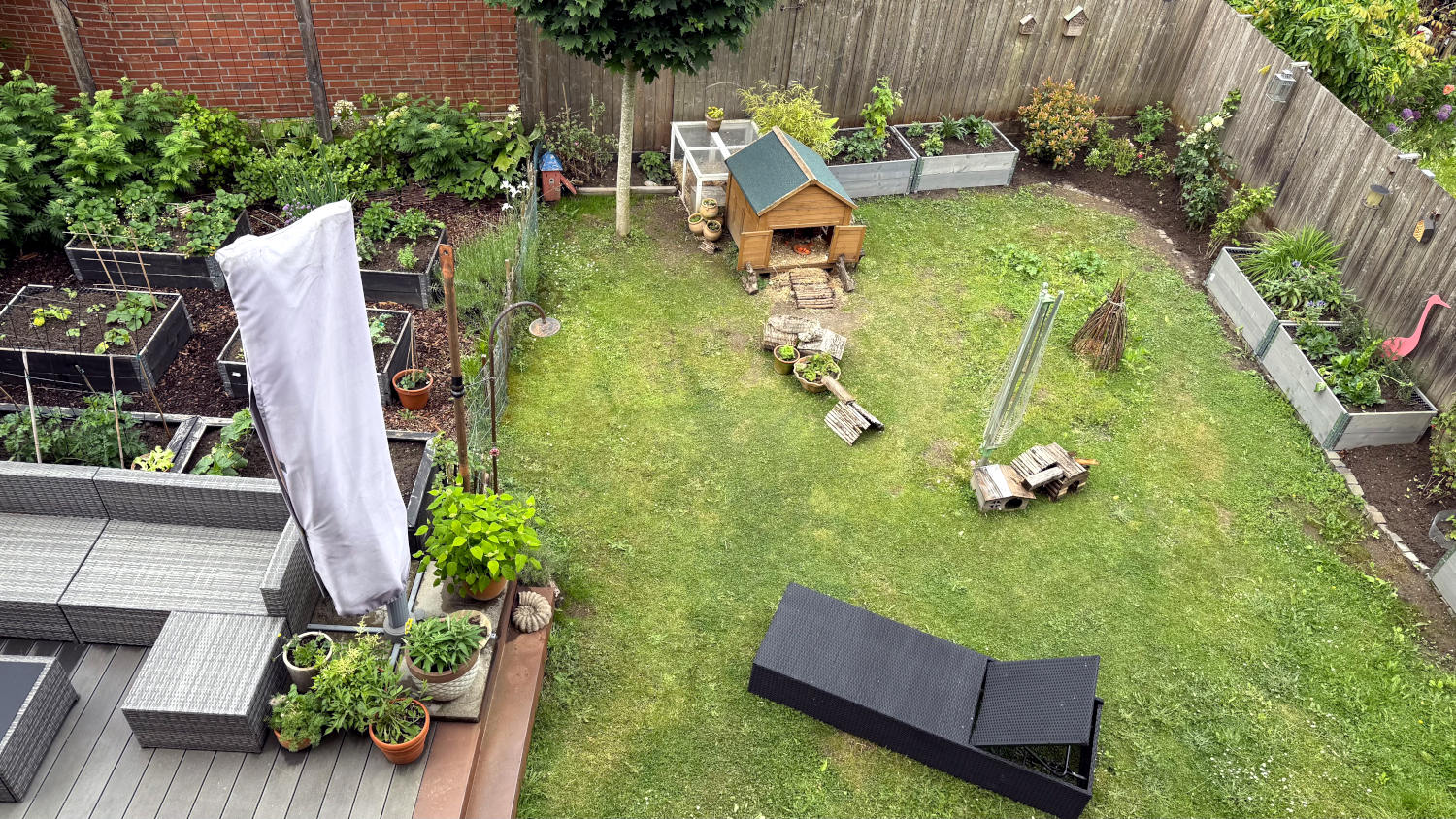 Blick aus dem ersten Stock in den Garten: Rasenfläche mit Meerschweinhäusern und einer Liege, an den Rändern Hochbeete und Büsche, links deutet sich ein Gemüsegarten an
