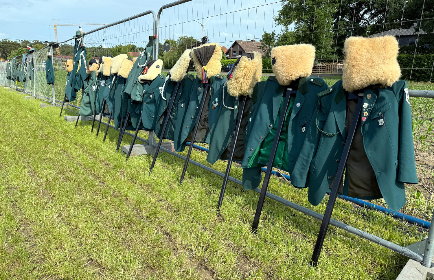 Schützenjacken und -Mützen auf Ständern an einem Bauzaun