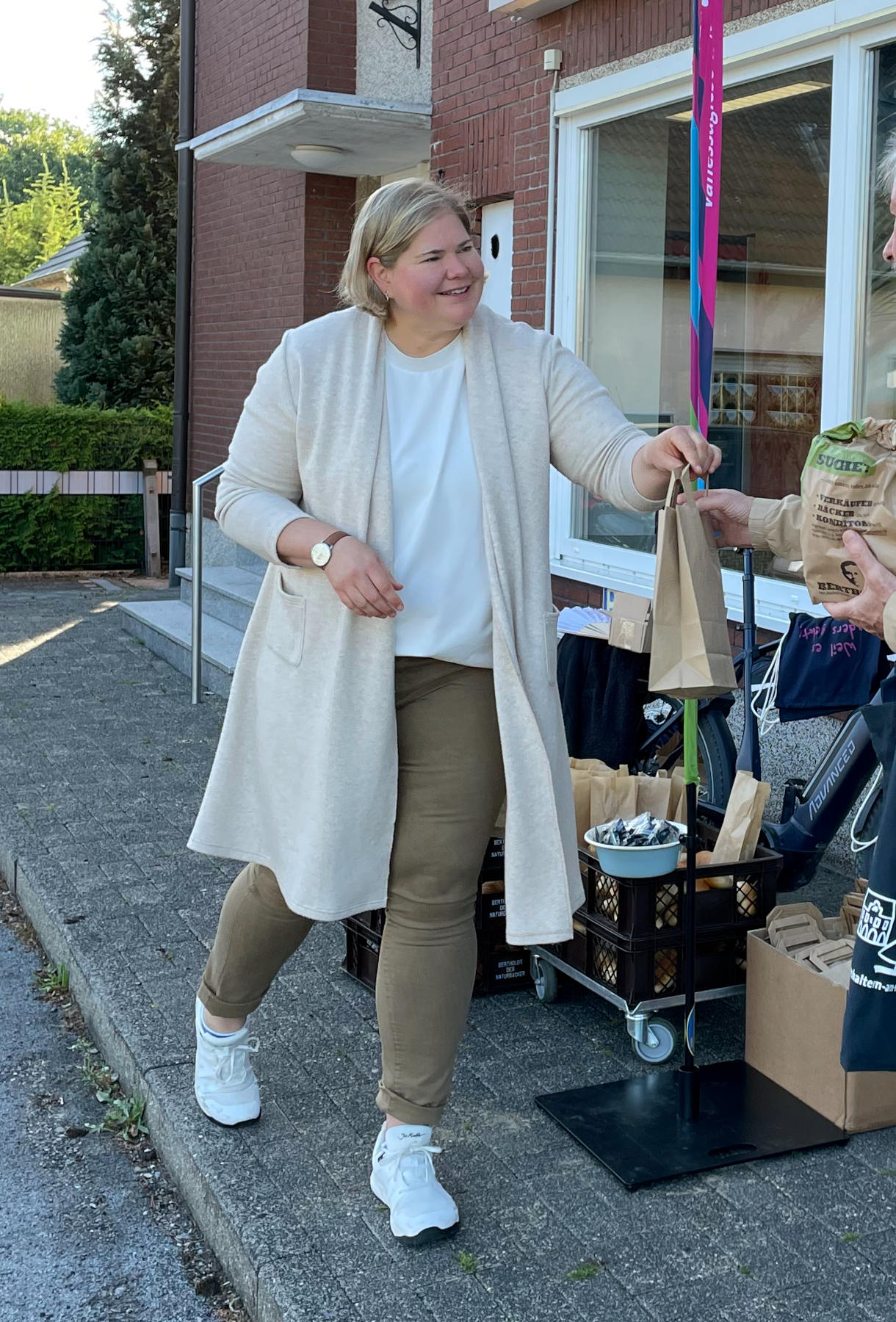 Vanessa steht neben Rollwagen mit Brötchen gibt einer Person außerhalb des Bildes eine Tüte.