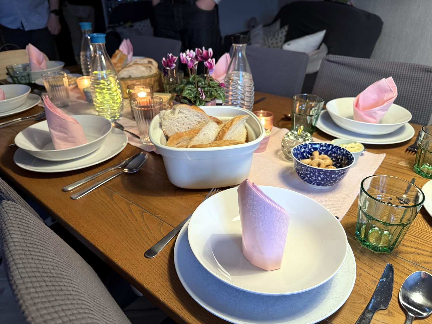 Gedeckter Tisch: Teller, Suppenteller, Servietten, Brot und kleine Schüsselchen, dazwischen Waserflaschen