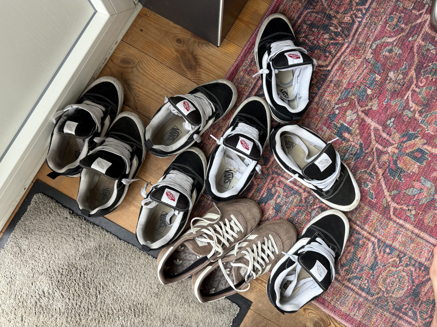 Vier Paare schwarz-weiße Vans-Schuhe, ein Paar Adidas auf einem Teppich.
