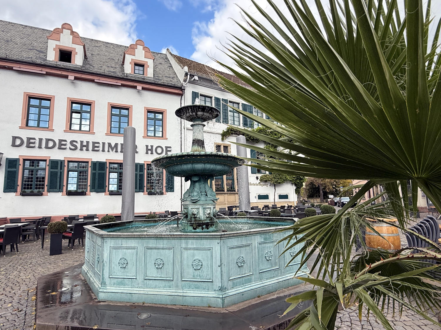 Deidesheimer Hof, traditionelle Architektur, davor ein Brunnen und eine Palme