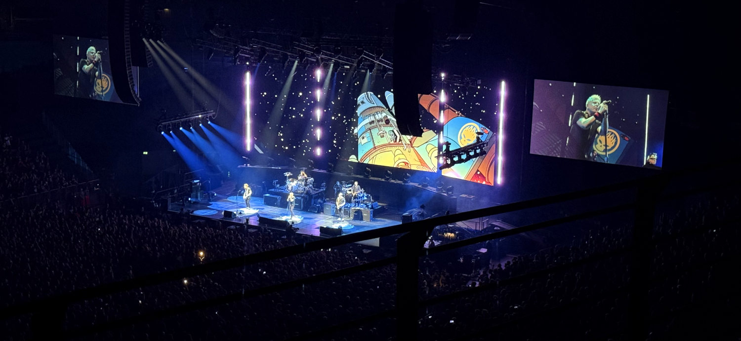 Blick vom Oberrang auf die Konzertbühne. Der Saal ist dunkel. Auf der Bühne Musiker, dahinter eine Leinwand mit einer bunten Zeichentrickrakete