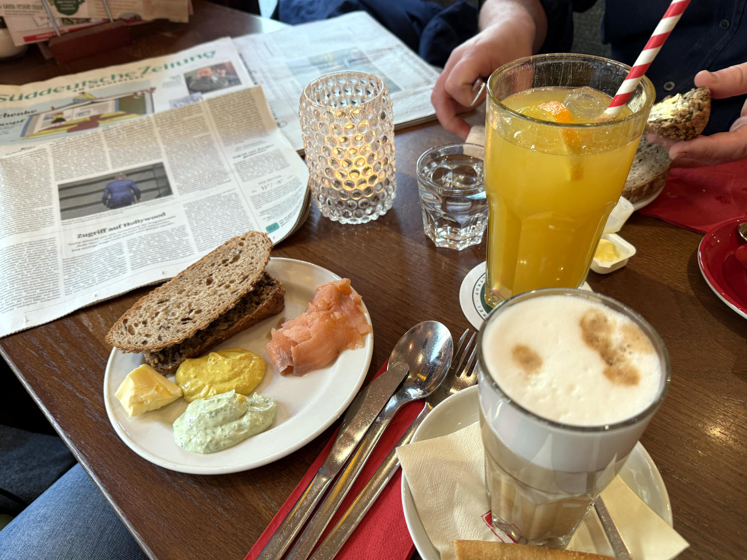 Frühstückstisch mit brotschwweiben, Dips und Lacks, großer Saftschorle und Latte Macchiato, daneben eine Süddeutsche Zeitung