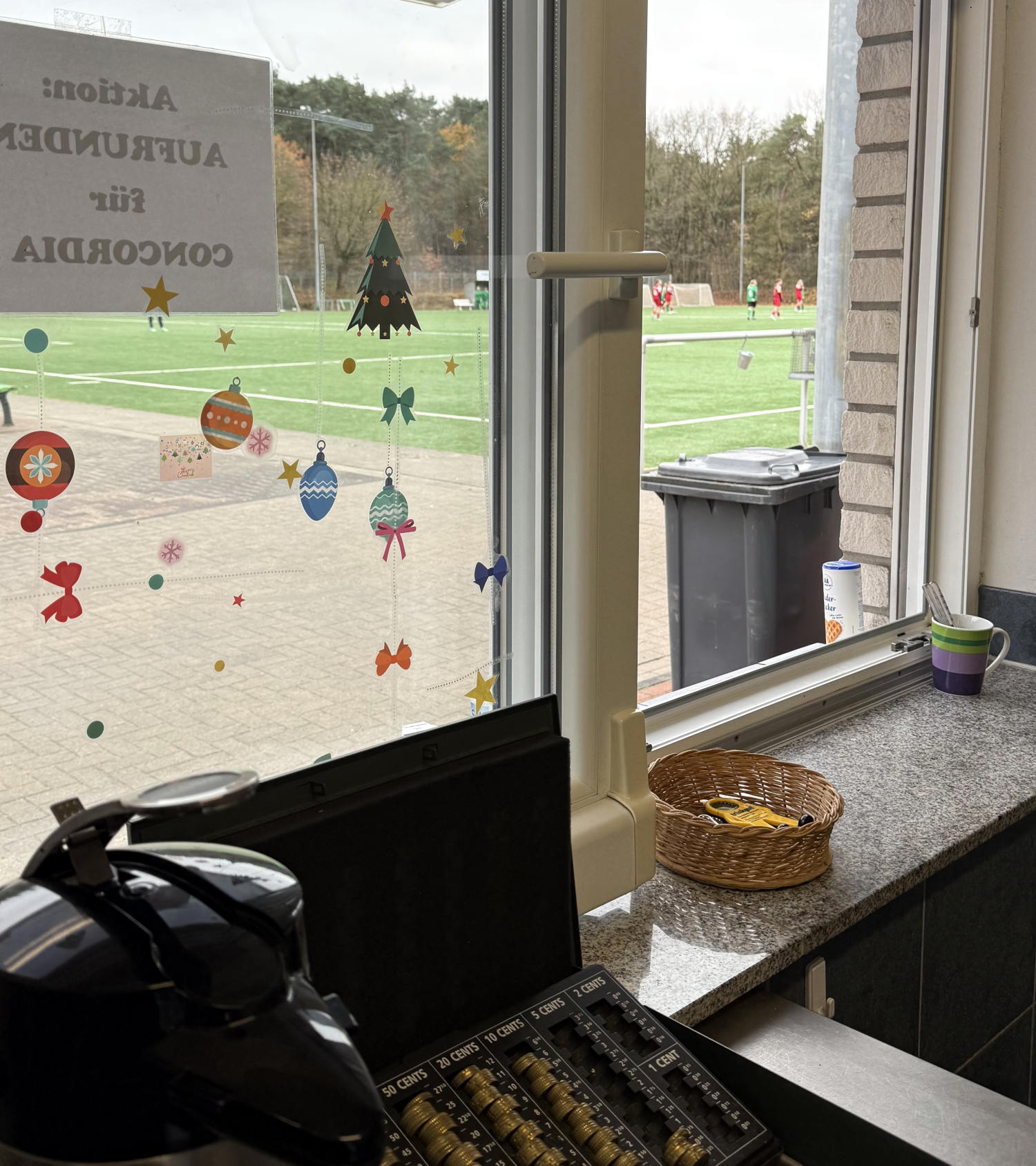 Blick aus einem geöffneten Schiebefenster auf einen Sportplatz. Am Fenster ist Weihnachtsdeko.