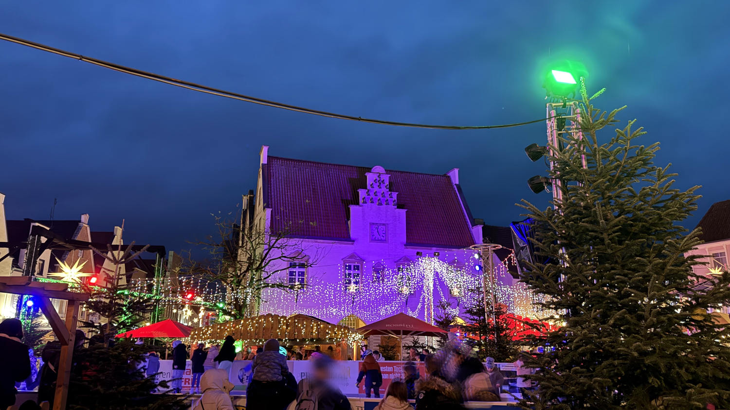 Ein historisches Rathaus, davor Lichterketten und eine EIsbahn. Menschen. Es ist dämmrig.