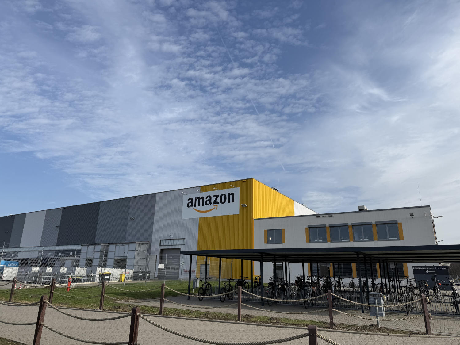 Amazon-Verteilzentrum in Dortmund: eine Hallo mit Amazon-Logo unter blauem Himmel, davor Fahrräder in einem Unterstand