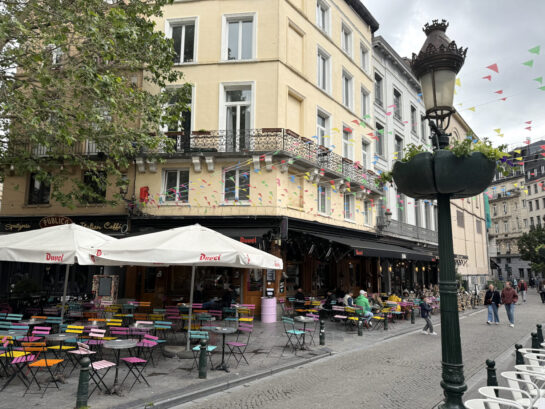 Straße in der Brüsseler Altstadt: eine Hastronomie, Fähnchen, bunte Stühle drau0en. 