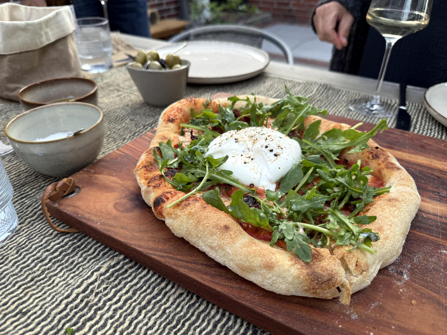 Eine Pizza mir dickem, knusprig-fluffigem Rand, Rucole und Büffelmozzarella auf einem Holzbrett