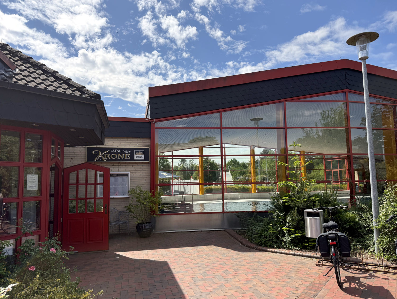 Ein Gebäude mit Glasfront, darin ein kleines Hallenbad, daneben das Restaurant Krone. Das Gebäude ist Rot-Gelb und hat den Charme der 80er Jahre.
