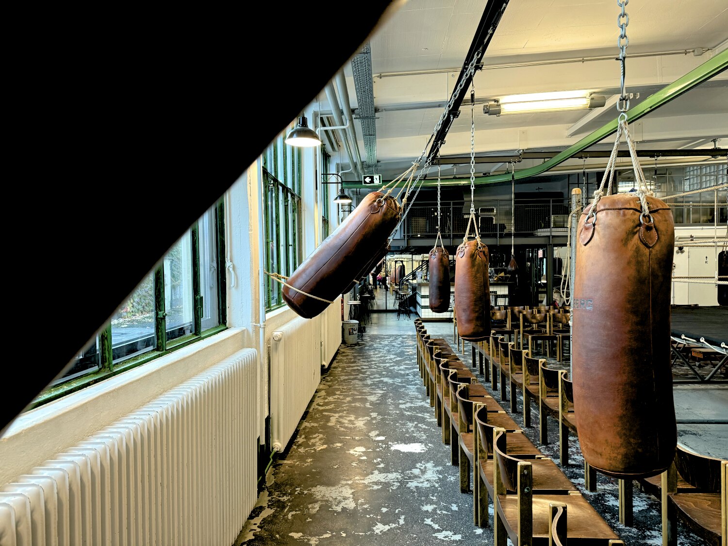 Lederne Boxsäcke hängen von der Decke, rechts Stühle, am Ende ein Spiegel und eine Bar.